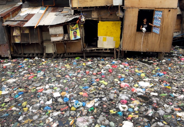 Một phụ nữ đổ nước xuống dòng sông ô nhiễm tại khu ổ chuột ở Manila, Philippines.