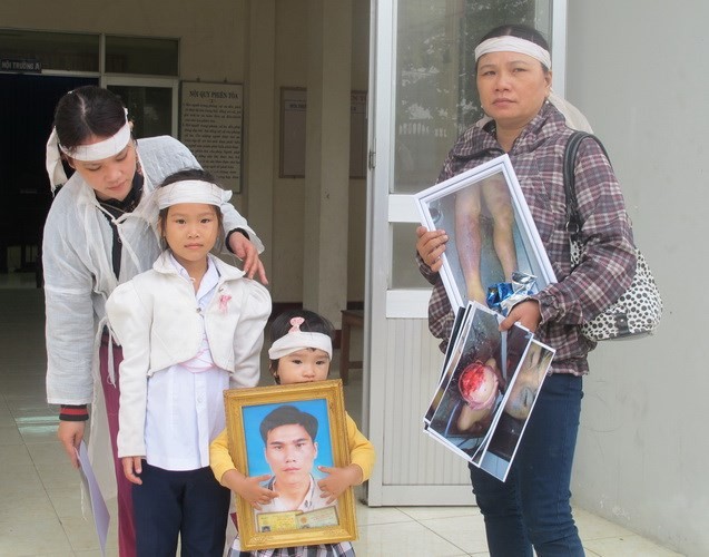 Kim Oanh ôm di ảnh của cha. Bên cạnh em, bác ruột và mẹ cầm những bức ảnh chụp các vết thương của anh Kiều khi bị các công an đánh.