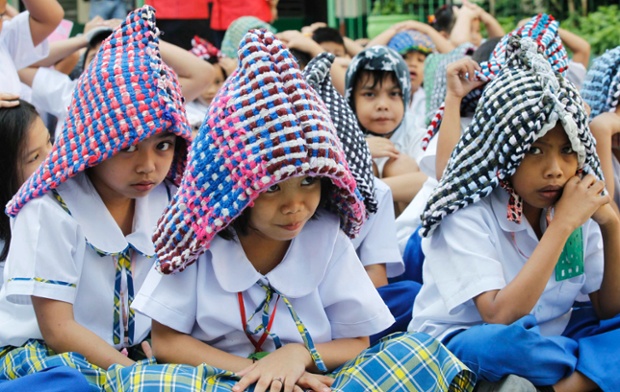 Học sinh tiểu học sử dụng thảm chùi chân như một thiết bị bảo vệ đầu trong cuộc diễn tập chống động đất ở Paranaque, Philippines.