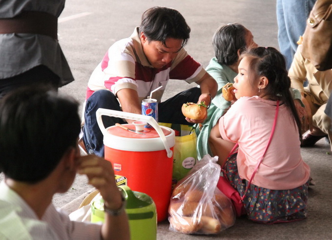 Một gia đình mang theo nước uống và bánh mì để ăn lót dạ để đón người thân về quê ăn tết tại ga quốc tế. Ảnh: Hữu Khoa
