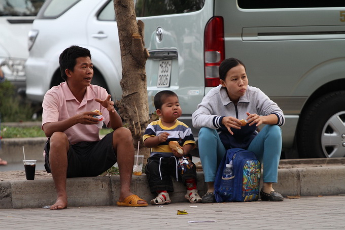 Gia đình anh Nguyễn Văn Lan ăn tạm ổ bánh mì chờ đến giờ lên máy bay về quê ăn tết. Ảnh: Hữu Khoa