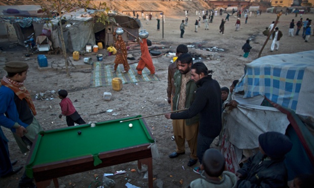 Những phụ nữ Pakistan đội nước trên đầu trong khi qua một nhóm đàn ông chơi bi-a tại một khu ổ chuột ở Rawalpindi.