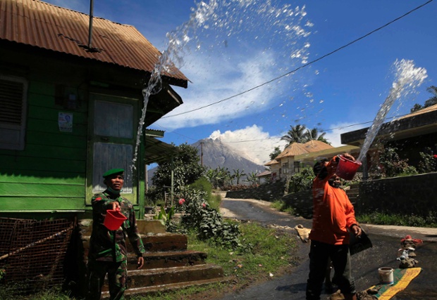 Binh sĩ và người dân té nước vào một ngôi nhà khi núi lửa Sinabung tiếp tục phun trào tro bụi tại North Sumatra, Indonesia.