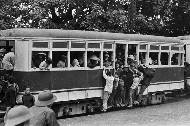 7. 23 Mar 1973, Hanoi, North Vietnam --- Clang goes the trolley. Maybe there isnt too much clanging but theres a lot of clinging as a trolley moves through Hanoi recently. Youngsters who cant get in, get on. The conductor, wearing a helmet, seems unusually pleasant in such a situation. UPI correspondents Tracey Wood and Marie Grebenc, who visited Hanoi recently, both noted the presence of many Merry looking children. The children are back in Hanoi now that the sease-fire is in effect. Before, many children had been evacuated from the city. --- Image by © Bettmann/CORBIS