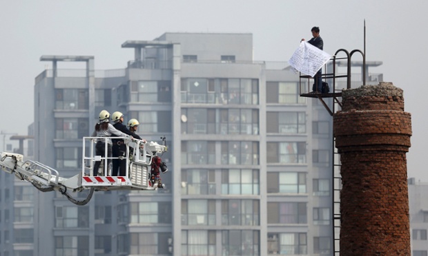 Nhưỡng người thương thuyết đưng trên một chiếc thang nói chuyện với một người đàn ông cầm đơn kiện đứng trên ống khói ở Bắc Kinh, Trung Quốc.