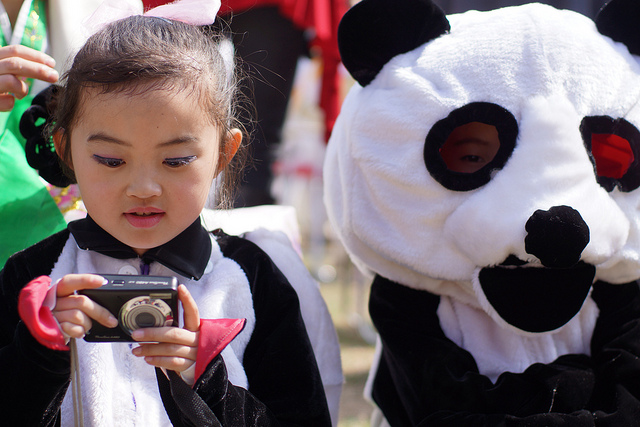  	Một cô bé trong trang phục gấu trúc đang xem lại ảnh được chụp bằng máy kỹ thuật số sau khi trình diễn trong một hội chợ dân gian nhân Ngày Mặt Trời, kỉ niệm 100 năm ngày sinh của cố Chủ tịch Kim Nhật Thành.