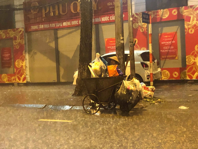 Chạnh lòng với hình ảnh cô lao công dọn rác bên lề đường trong đêm 30 Tết mưa bão - Ảnh 1.