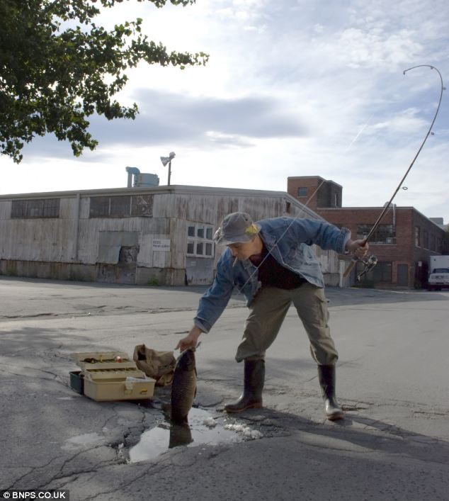 A fisherman in Wellington Boots catches a fish in a pothole disguised as a pond