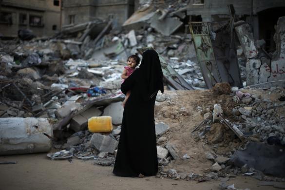 Một người phụ nữ Palestine bế con gái đứng trước ngôi nhà bị phá hủy trong một cuộc tấn công của Israel nhằm vào dải Gaza. 
