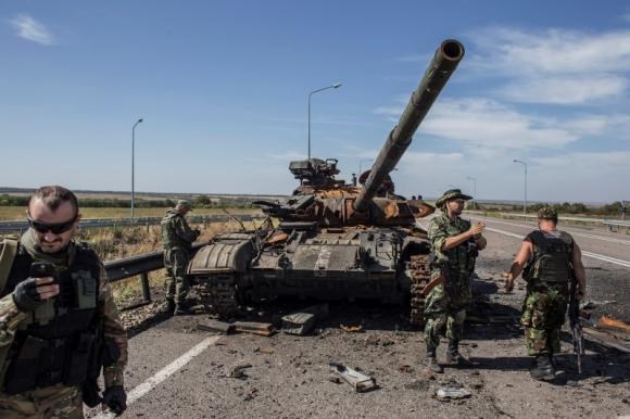 Quân ly khai Ukraine đứng cạnh một xác của chiếc xe tăng của quân đội Kiev. Ảnh: Reuters.