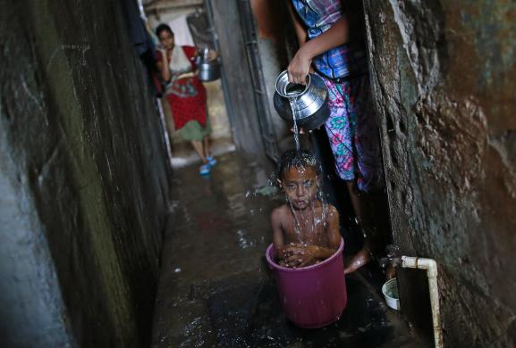 Cậu bé được mẹ tắm trong xô bên ngoài nhà tại một khu ổ chuột ở Mumbai, Ấn Độ.