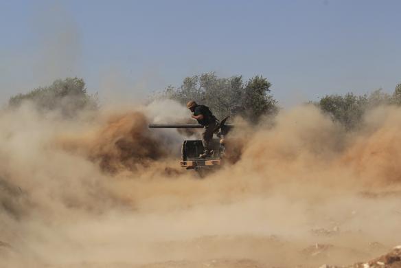 Chiến binh phiến quân Syria đứng giữa bụi và khói sau khi phóng rocket nhằm vào quân đội chính phủ ở Wadi Al-Dayf, tỉnh Idlib.