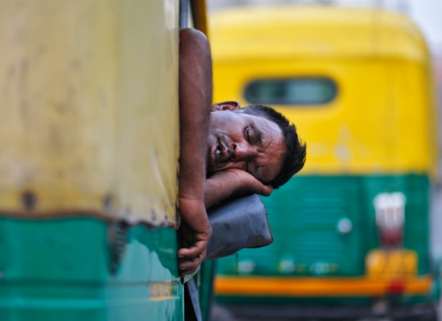 Một tài xế ngủ trên xe ba bánh trong khi chờ khách ở thành phố Delhi, Ấn Độ.