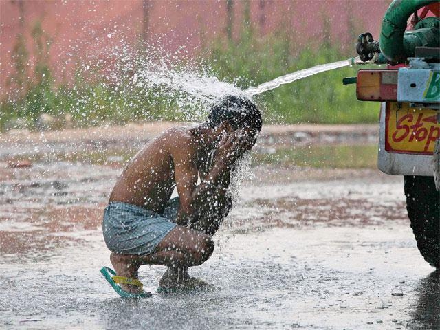 Một người đàn ông tắm dưới vòi của xe chở nước dưới trời nắng nóng ở ngoại ô thành phố Jammu, Ấn Độ.