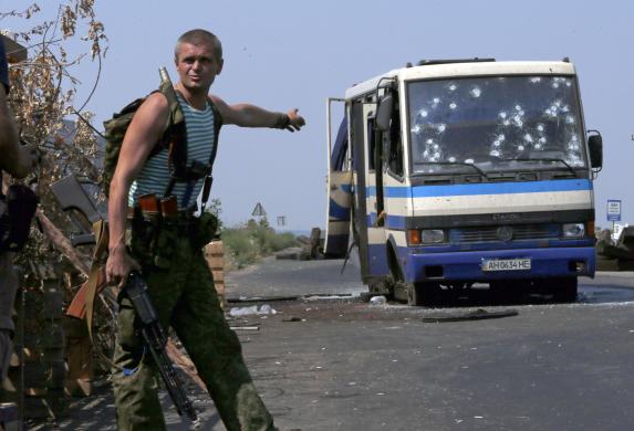 Một tay súng ly khai có vũ trang của Ukraine chỉ vào một chiếc xe bus bị đạn bắn thủng lỗ chỗ đang đỗ tại trạm kiểm soát ở ngoại ô Donetsk.