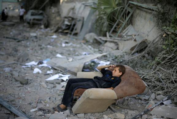 Cậu bé người Palestine ngồi trên ghế sofa bên ngoài ngôi nhà bị phá hủy trong cuộc không kích của quân đội Israel nhằm vào thành phố Gaza.