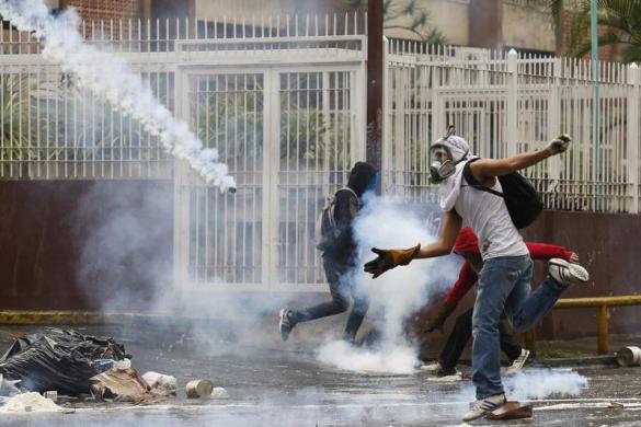 Một người biểu tình chống chính phủ cố gắng bắt lựu đạn hơi cay do cảnh sát ném trên đường phố ở Caracas, Venezuela.