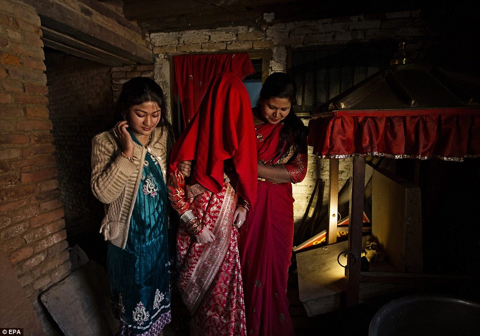 Mẹ Purna Shova Bajracharya (R) và cháu trai em gái của Samita Bajracharya (C) giữ cô khi cô được đưa ra ngoài với khuôn mặt của cô được bao phủ bởi một miếng vải và mặc một chiếc váy cưới truyền thống để thờ mặt trời trong một buổi lễ Gufa tại Ratnakar Mahavihar trong Patan, Nepal