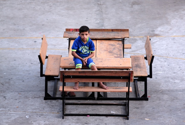 Cậu bé người Palestine ngồi trong sân của một trường học LHQ ở Gaza, nơi gia đình cậu bé đang sơ tán.