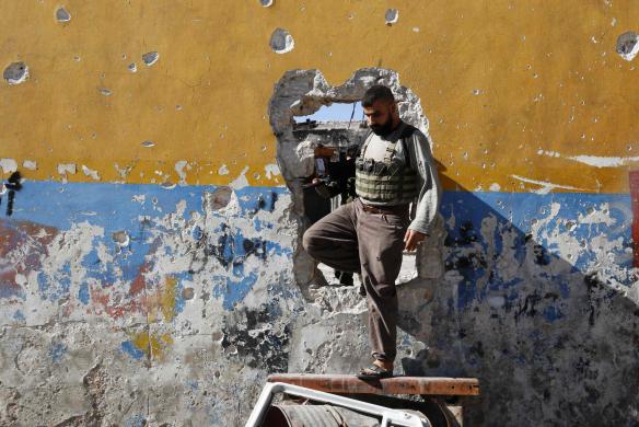 Một chiến binh phiến quân đi qua lỗ trên tường tại thành phố Ramouseh, Syria.