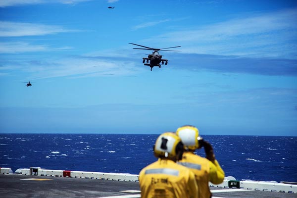 Biến thể trực thăng tấn công AH-64E đang tiến vào khu vực hạ cánh trên boong tàu đổ bộ tấn công dưới sự hướng dẫn của nhân viên điều phối trên tàu.