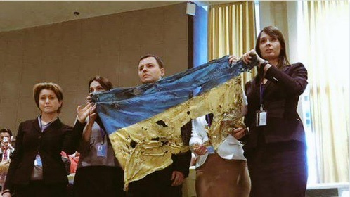 
Nhóm đại biểu Ukraine giơ lên lá quốc kỳ rách tả tơi trong khi Tổng thống Putin phát biểu.
