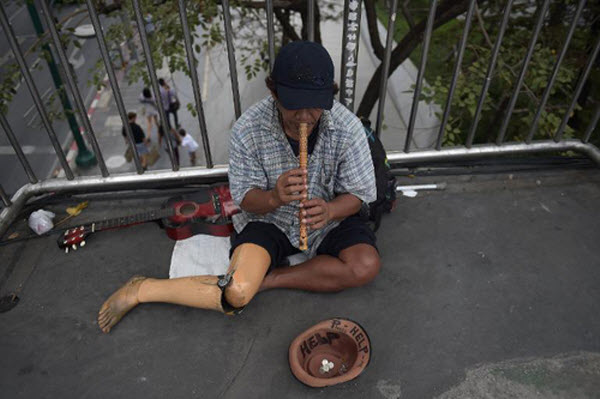 Người đàn ông đeo chân giả đang thổi sáo để xin tiền ở một cầu vượt trên cao tại Bangkok, Thái Lan.