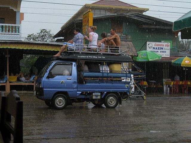 Thời tiết mưa và ẩm ướt không ngăn du khách đến thăm thị trấn Vang Vieng nổi tiếng tại thủ đô Viên Chăn. Ở Việt Nam chúng ta hiếm khi gặp người ngồi trên thùng xe tải hoặc xe bán tải khi tham gia giao thông, nhưng ở giữa thủ đô Viên Chăn các bạn sẽ bắt gặp thường xuyên những cảnh tượng đó.Trên hình là Songthaew - có nghĩa là hai hàng với 2 băng ghế sau cho khách du lịch.