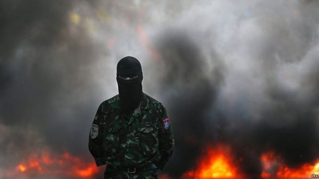 Một quân tình nguyện chính phủ đứng trước đám khói lửa do đốt lốp xe trong cuộc biểu tình. Ảnh: EPA