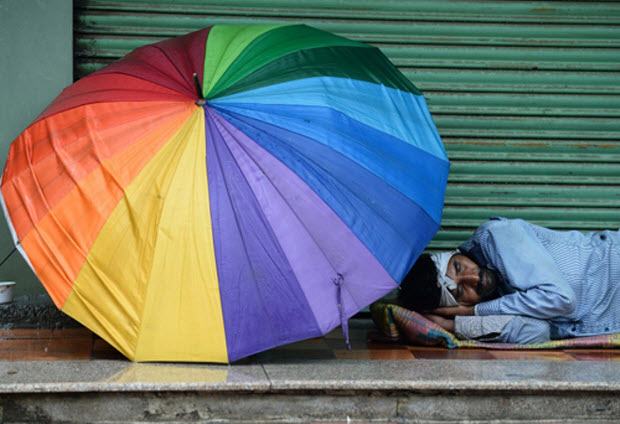 hân viên bảo vệ tư nhân ngủ bên ngoài một cửa hàng đã đóng cửa dưới cơn mưa ở New Delhi, Ấn Độ.