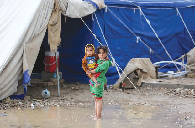 Bé gái tị nạn bế em đứng trong khu trại ngập nước sau một trận mưa lớn ở thành phố Baghdad, Iraq.