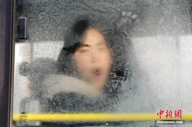 
Một người phụ nữ đằng sau cửa kính băng giá của xe bus.
