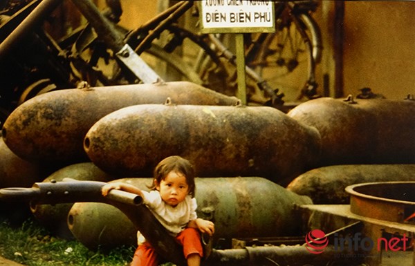 Một em nhỏ chơi bên đống vũ khí sau chiến tranh.