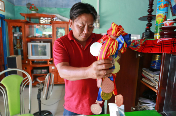 Ông Nguyễn Văn Biểu cùng với những tấm huy chương trong nước và quốc tế mà cô con gái Nguyễn Thị Thu Thùy giành được.