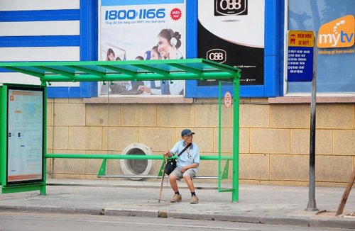 Một người đàn ông ngồi chờ xe buýt trên đường Đinh Tiên Hoàng vào lúc sáng sớm.
