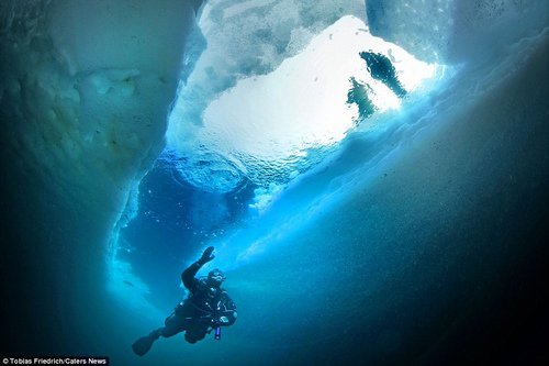 Một thợ lặn chui xuống bên dưới tảng băng nổi thông qua một khe nứt.