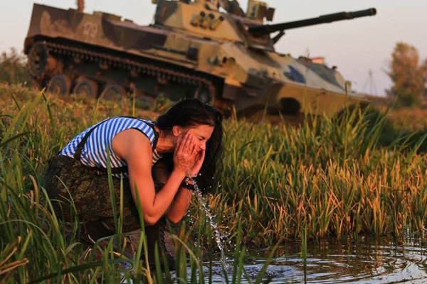 Nữ lính dù rửa mặt bên dòng suối trong lúc hành quân, phía xa là xe chiến đấu đổ bộ đường không BMD-4, vũ khí quen thuộc của lính dù Nga.