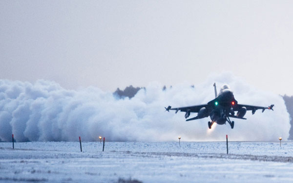 
Sức mạnh từ động cơ phản lực trên tiêm kích F-16 thổi tuyết trên đường băng bay mù mịt khi nó cất cánh vọt lên cao.
