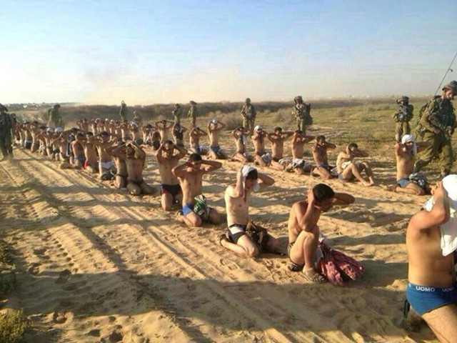 Các binh sĩ Israel đứng canh giữ những người Palestine bị bắt giữ trong chiến dịch tấn công quân sự vào Dải Gaza.
