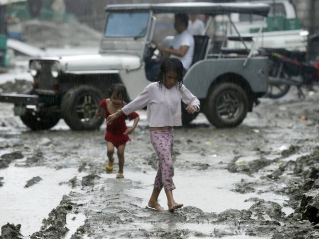 Trẻ em đi trên đường bùn đất dưới trời mưa do bão Matmo gây ra tại thành phố Manila, Philippines.