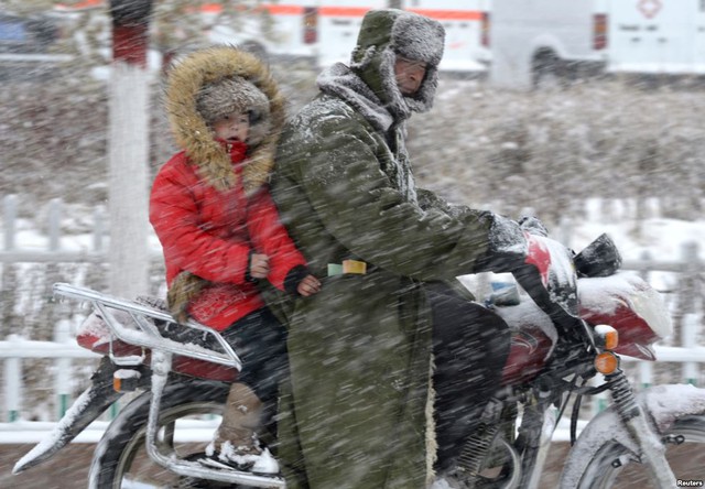 Người đàn ông đi xe máy chở một em bé phía sau trong bão tuyết ở Balikun, Khu tự trị Tân Cương, Trung Quốc.