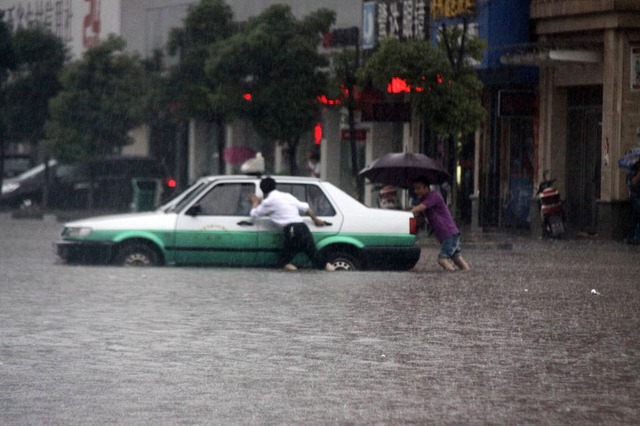 Tài xế và hành khách đẩy một chiếc xe taxi mắc kẹt trên đường phố ngập lụt sau mưa lớn ở Thụy Xương, tỉnh Giang Tây, Trung Quốc.