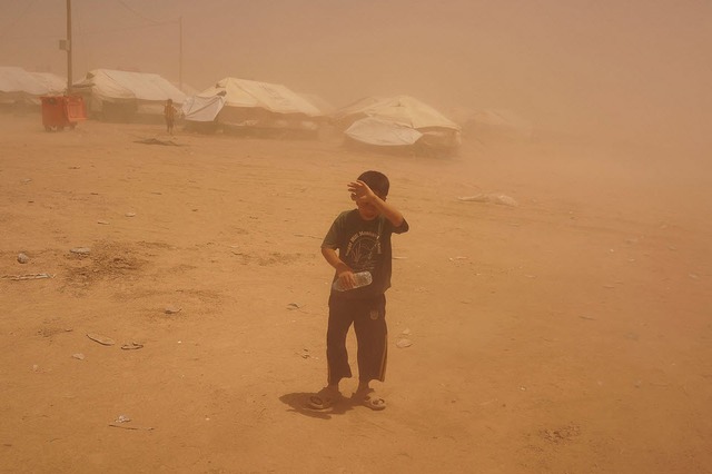 Một cậu bé đi trong bão cát tại trại tị nạn Khazair ở Iraq.