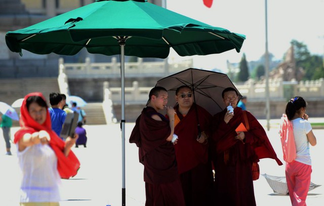 Các nhà sư tránh nắng nóng dưới một chiếc ô lớn khi tham quan quảng trường Thiên An Môn ở Bắc Kinh, Trung Quốc.