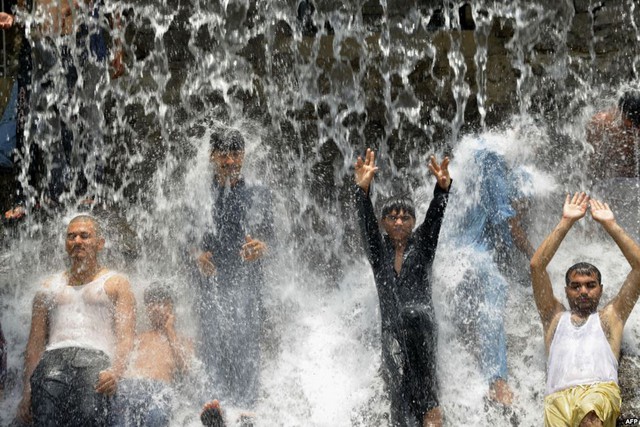 Các thanh niên tắm dưới thác nước để tránh nóng trong một công viên ở Lahore, Pakistan.