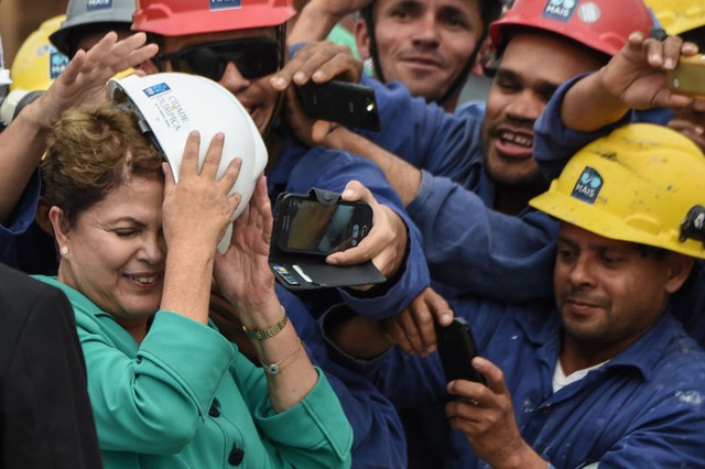 Tổng thống Brazil Dilma Rousseff lấy mũ bảo hộ che mặt khi các công nhân cố gắng chụp ảnh bà tại công trường xây dựng công viên Olympic Rio 2014.