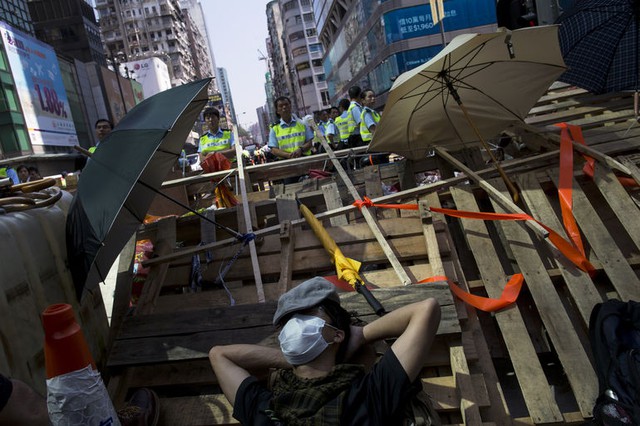 Người biểu tình ngủ trên hàng rào chắn trong khi cảnh sát đứng bảo vệ phía sau tại khu phố tương mại Mongkok, Hong Kong.