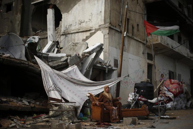 Người phụ nữ Palestine ngồi bên ngoài túp lều tạm cạnh tòa nhà đổ nát do trúng đạn pháo của Israel tại thị trấn Beit Hanoun, Dải Gaza.