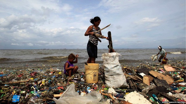 Một phụ nữ và con nhỏ nhặt củi và đồ phế liệu trôi dạt vào bờ biển Vịnh Manila tại khu ổ chuột Baseco, Philippines.