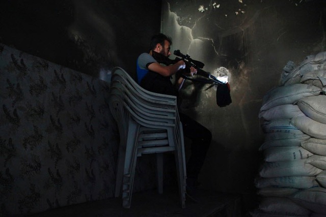 Chiến binh phiến quân Syria chĩa súng bắn tỉa qua lỗ trên tường tại thành phố Aleppo.